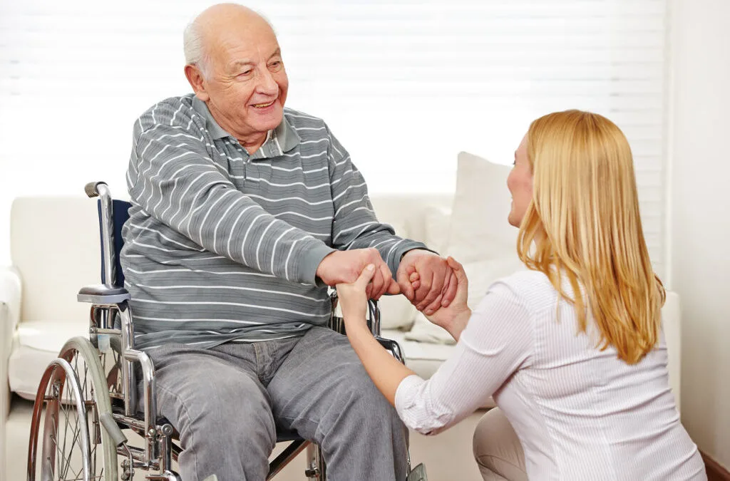 Caregiver holding the hand of an older man in a wheelchair